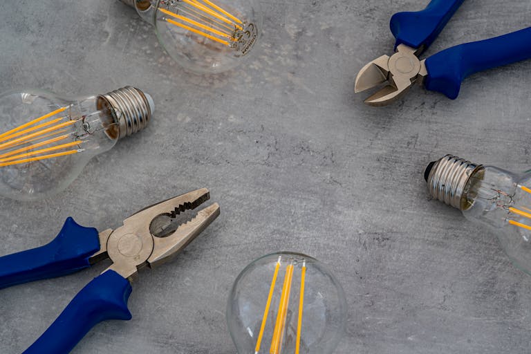 A flat lay of vintage Edison bulbs and pliers on a gray surface, emphasizing industrial design.